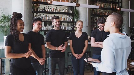 Female restaurant bar manager holding digital tablet giving motivational talk to waiting staff before opening - shot in slow motion