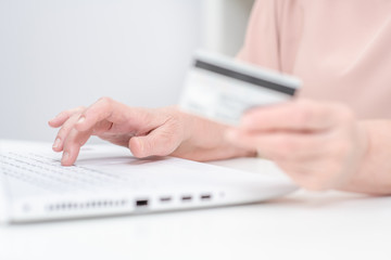 Hands of an senior woman hold credit card and use laptop. Online shopping
