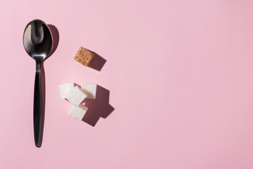 square pieces of cane sugar and a metal spoon on a pink background