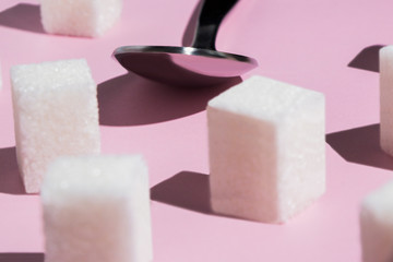 square pieces of cane sugar and a metal spoon on a pink background