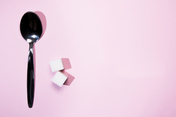 square pieces of cane sugar and a metal spoon on a pink background