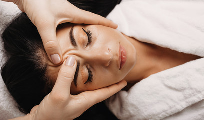 Caucasian girl with black hair who is sleeping during a facial massage at spa