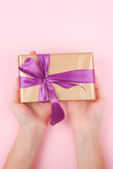 Gift wrap in the hands of a girl, top view. Flat lay on pink background, Woman gives a present for Christmas or birthday - web banner