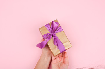 gift box on a pink background. A gift in female hands. Flat lay style. Gold packaging with purple bow.