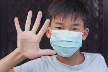 Asian preteen boy wearing medical face mask and making stop sign, self-quarantine, social...