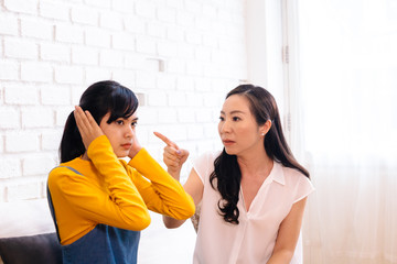Argument between annoyed Asian teenage daughter and upset middle aged mother. The child covering ears while mum pointing finger at. Bad, unhealthy, toxic family relationship concept
