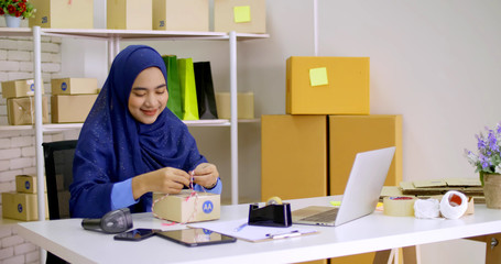Beautiful muslim female merchandiser preparing parcel at the office.