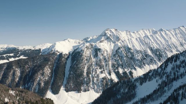 AERIAL: Amazing mountainous landscape with high peaks and snow. Green trees on the slopes. Zillertal, Austria