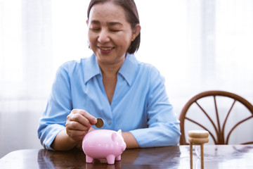 Obraz na płótnie Canvas Asain Elder putting coin money to piggy bank saving, family, savings, age and people concept - smiling senior couple with money and piggy bank at home.