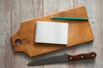 The kitchen composition. An old cutting board, a chef's knife, a Notepad for writing recipes and a pencil on a light wooden background.