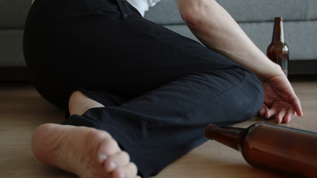 Young drunk man lies on a floor and a beer bottle on a floor near