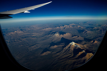 Naklejka na ściany i meble Fantastic night view of the Andes mountain range backlit under the wing of an airplane shot from a great height. View into the porthole. Background. Scenery. Concept.