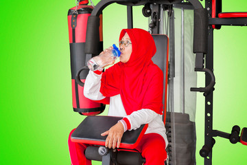 Senior woman drinking water on the gym machine