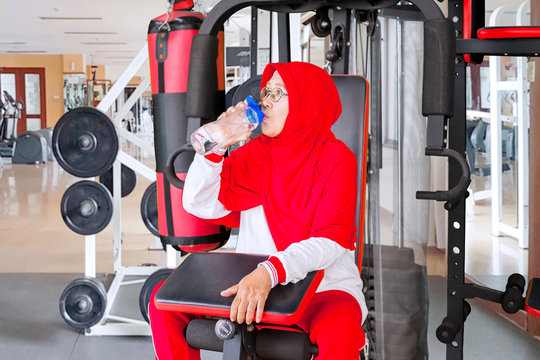 Senior woman sits on gym machine while drinking
