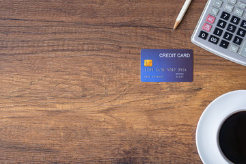 Top view of a blue credit card, pencil, calculator, coffee cup on wooden table in office. Space for...