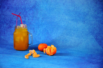 Glass mug of citrus juice with ice and slices of ripe mandarin next to a blue background. © Алексей Желтухин