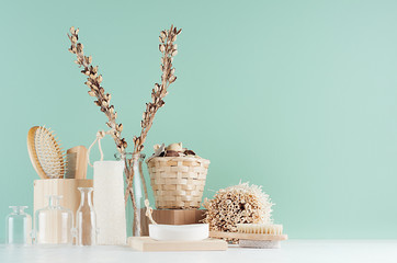 Natural beige wooden cosmetics accessories in green mint menthe bathroom interior - bath sponge, soap, dried plant, glass bottles on white wood board.