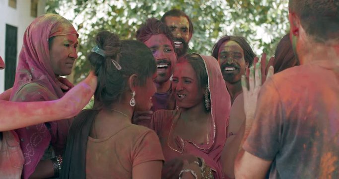 White tourist couple celebrating festival Holi in India looking at camera pose photo video selfie and join playing dancing celebrating with locals blurred out-of-focus background bokeh, slow-motion
