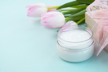 Fototapeta na wymiar Cosmetic cream in a jar, gift box and flowers tulips on light blue background. Concept beauty, skincare, gifts and discount. Close up, copy space