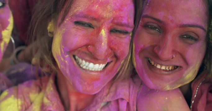 Happy gregarious smiling toothy multiethnic women, Indian and white western tourists having the time of their lives playing celebrating Holi festival, hugging together tight bonding cheerful pose