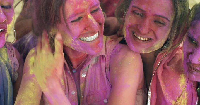 Happy gregarious smiling toothy multiethnic women, Indian and white western tourists having the time of their lives playing celebrating Holi festival, hugging together tight bonding cheerful pose