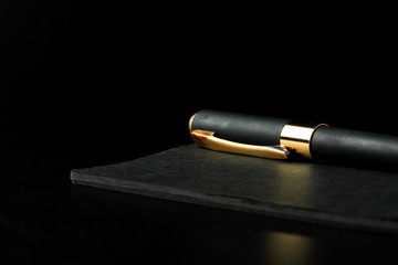Black notepad with pen on black table close up