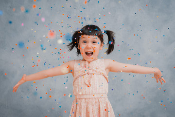 little girl child cheerfully throws up colorful tinsel and confetti on a gray blue background.