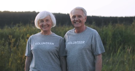 Portrait of Caucasian happy married couple of old male and female eco volunteers looking at each other with love and smiling to camera happily outdoor. Senior man and woman at cleaning day.