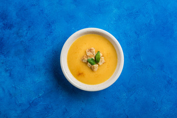 Pumpkin and carrot soup with cream and spinach with crackers on a classic blue background.