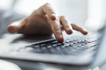 Male hands typing on laptop keyboard in sunny office, business and technology concept. Close up