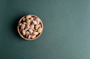pistachios in a wooden bowl on a dark green background, close up, copy space