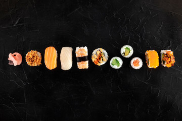 Sushi set, shot from the top on a black background. A flat lay of various maki, nigiri and rolls, with fish and vegetables, with a place for text