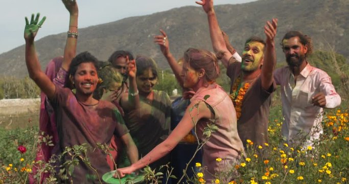 Multi ethnic mixed race couples brown white western, locals and tourists, enjoying themselves dancing making merry to celebrate Holi, India with colored faces in open fields of yellow marigold flowers