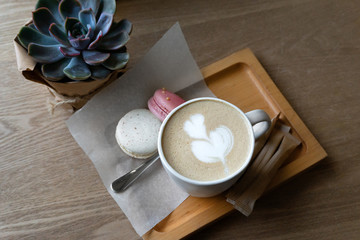 Cup of cappuccino coffee and macaroons on a wooden tray and table