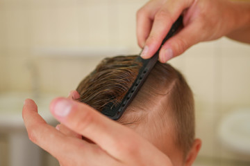 The hairdresser combs the boy with a black comb. Boy haircut