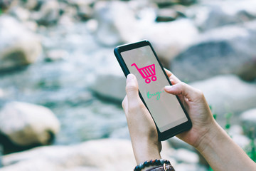 Women hand using smartphone do online business or shopping online in black friday with cart, dollar icons pop up in public area background.