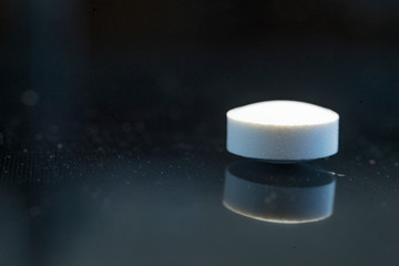 Pill on a dark background with reflection, healthy Vitamin supplementation concept,close up shot. Shallow depth of field. Macro.
