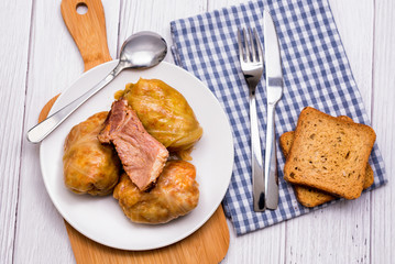 Cabbage rolls with meat, rice and vegetables in a white plate on a wooden table. Stuffed cabbage leaves with meat. Sarma, dolma, Chou farci, golubtsy or golabki.