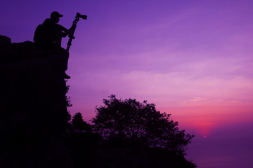 Photographer climbing on the top of the mountain to take a picture at sunset.