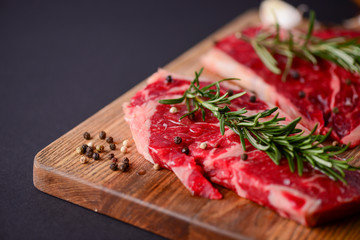 Fresh raw steak on wooden cutting board over black background with spices, top view.