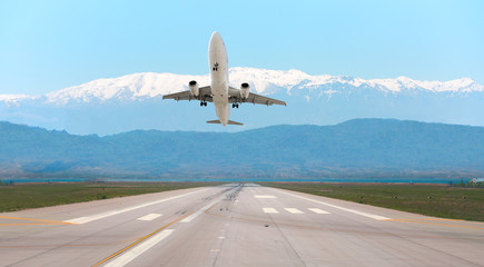 Fototapeta na wymiar White Passenger plane fly up over take-off runway from airport on the background snowy mountains