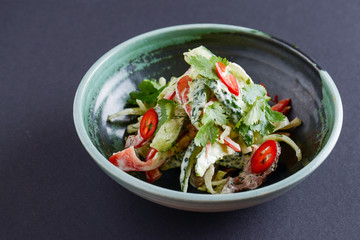 Healthy food. Ukrainian cuisine. Fresh green salad with cucumbers, pepper, parsley, dill and meat on black background