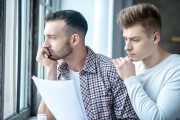 Two young men standing near the window looking desperate