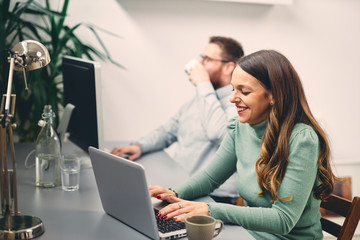 Two coworkers smiling and typing on computer in office.	