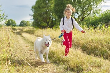 Little girl child running with white dog in meadow