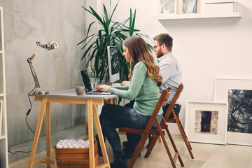 Two coworkers smiling and typing on computer in office.	