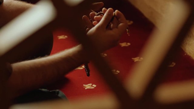 man who is cross-legged in the mosque and pulls the rosary. man who prays by prayer.man looking from behind the wooden motif.