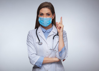 Doctor woman wearing medical mask and uniform pointing finger up.