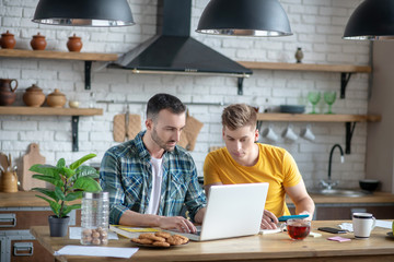 Two young men sitting in the kitching watching video tutorial