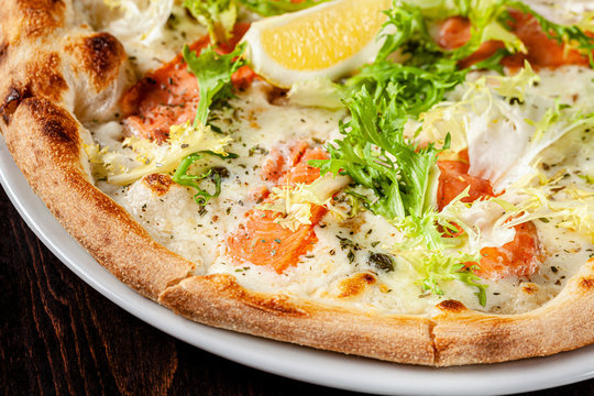 Italian cuisine. Thin pizza with large sides. Pizza with salmon, cheese sauce, lettuce. background image, copy space text